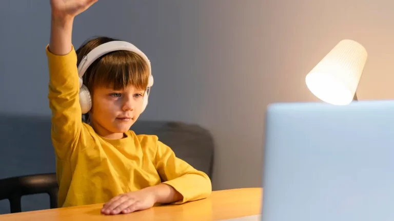 A boy raises his hand while sitting at a computer / Freepik