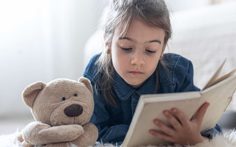 Girl reading a book with a teddy bear / Freepik