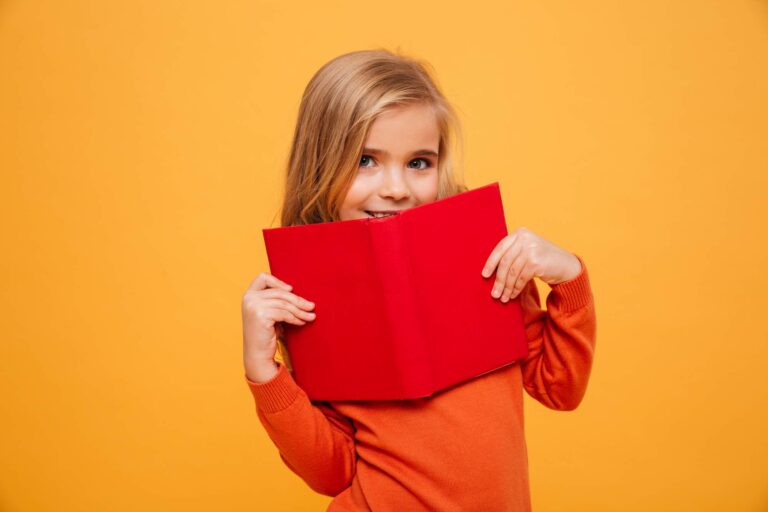 Girl smiling and hiding behind a book / Freepik