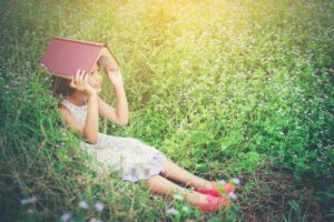 Девочка сидит на траве с книгой на голове летом / Freepik