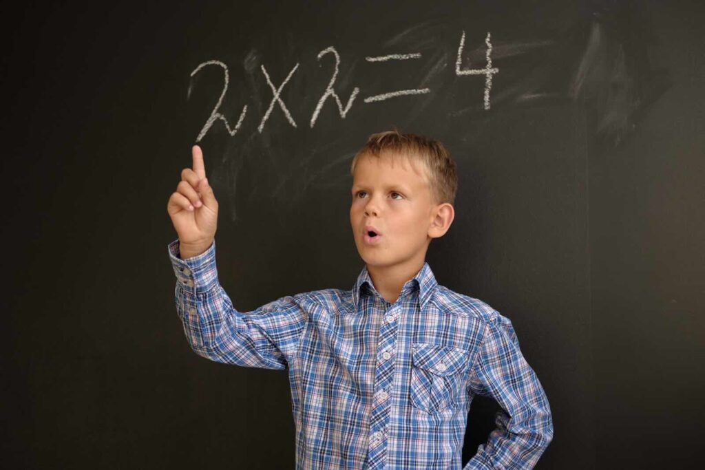 A European boy ponders solving a math problem while standing at the blackboard / Pexels