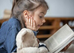 Little girl reading a book with her favorite toy / Freepik
