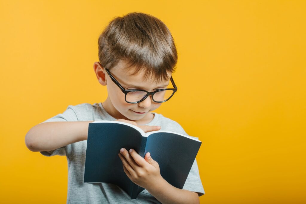 Boy with glasses reading a book / Freepik