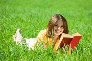 Девушка читает книгу лежа на траве летом / Freepik