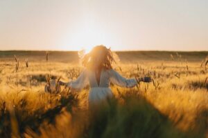 молодая красивая женщина с длинными светлыми волосами в белом платье на пшеничном поле ранним утром на рассвете. Лето - время мечтателей, развевающихся волос, женщина бежит по полю в лучах солнца. путешествия / Freepik