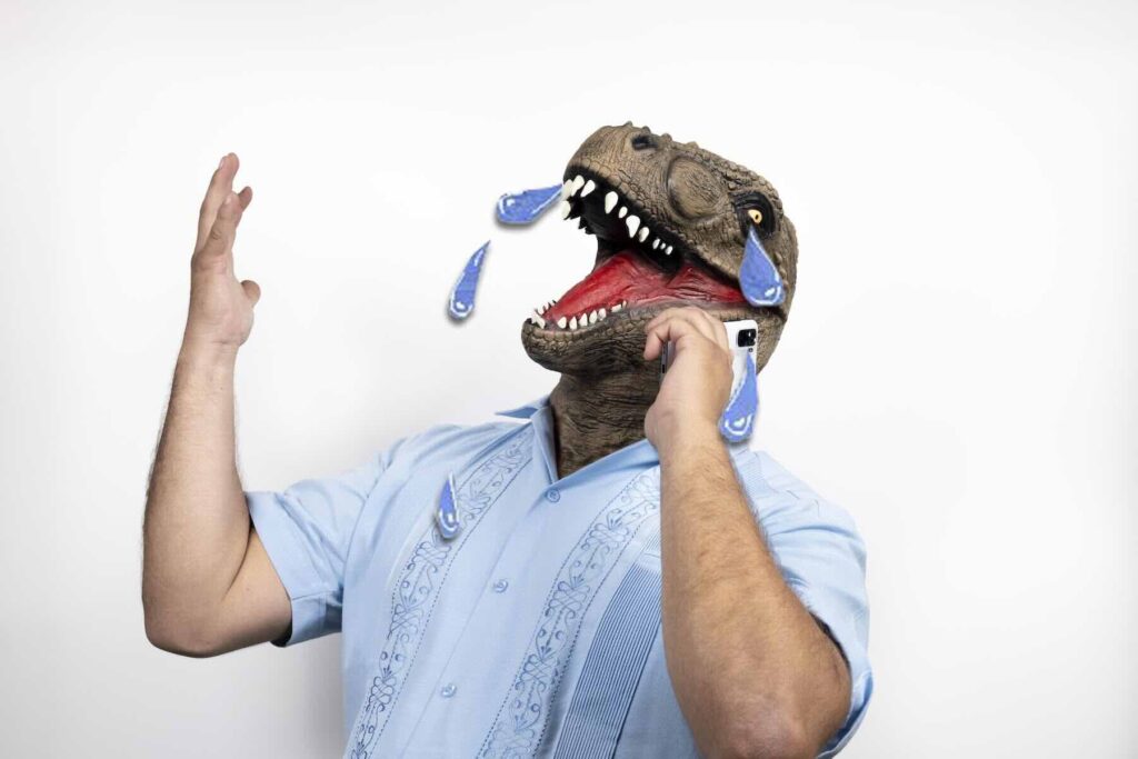 A man with a tyrannosaurus head talks on a smartphone and cries on an isolated white background / Freepik