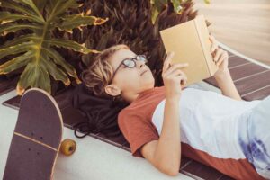Boy with glasses reading a book in the summer / Freepik