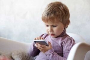 Ребенок сидит с телефоном на диване / Freepik
