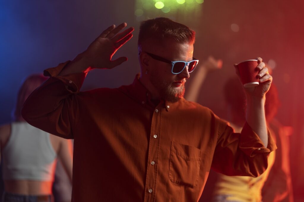 Парень в очках в клубе со стаканом напитка в руке