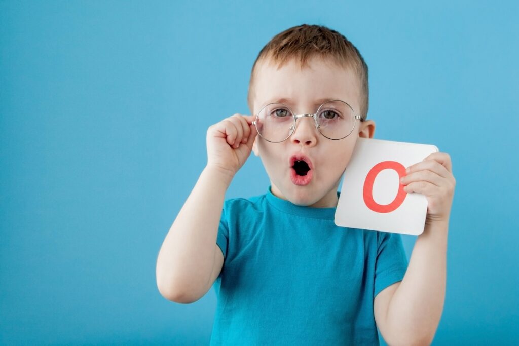 Милый маленький мальчик с буквой на синем фоне. Ребенок учит буквы. Алфавит.