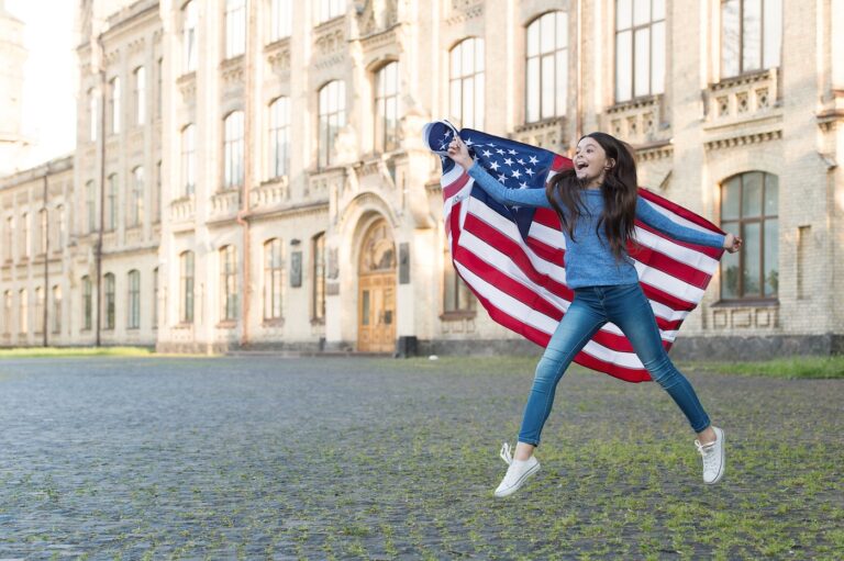 A little girl with an American flag in the background of outdoor architecture, a concept of introducing the USA.