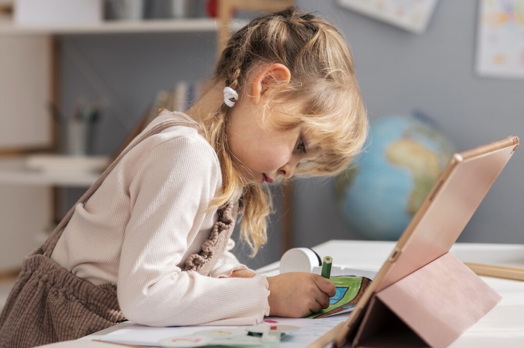 Девочка рисует на бумаге сидя перед iPad