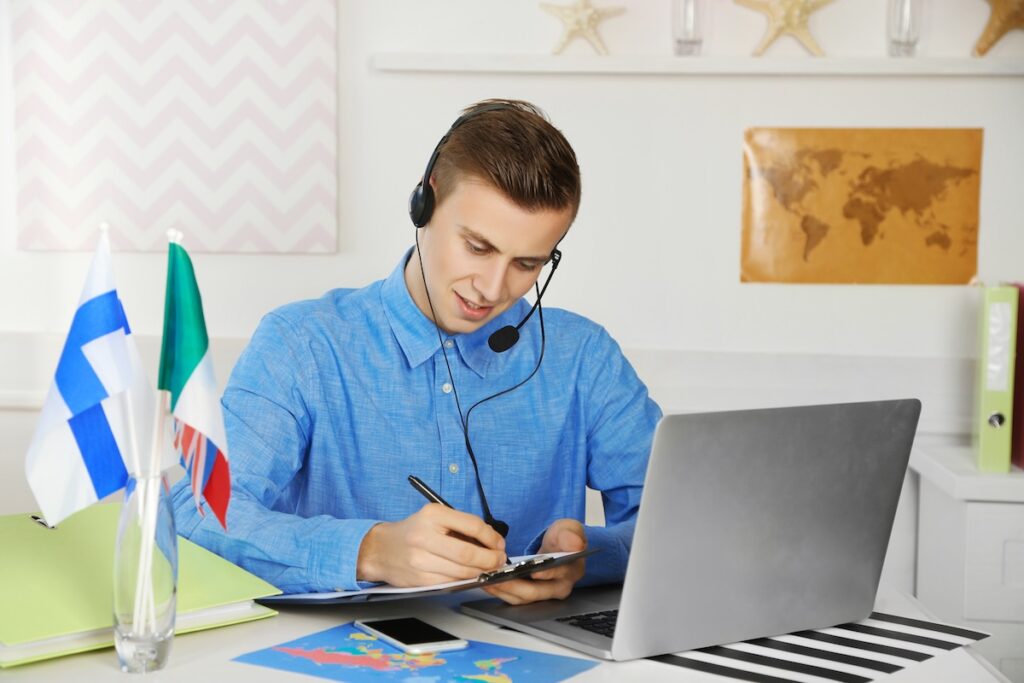 Young man talking on headset and making notes in the office of travel company
