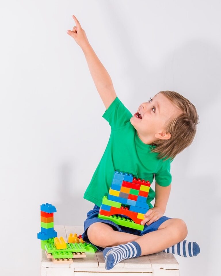 A little boy is playing a construction game with lots of colorful plastic blocks indoors.