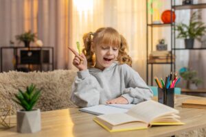 A young schoolgirl sits at a table on a couch, concentrating on a task in a notebook. A Caucasian child joyfully celebrates success, showing enthusiasm and joy as she completes her homework. Learning in Education.