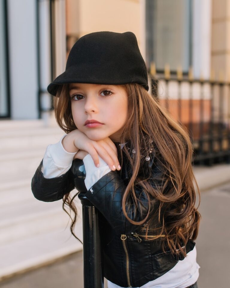 Bored cute little girl in a cute black hat is waiting for her mom on the street in front of a beauty salon. Beautiful long-haired brunette stands on the street with a sad expression on her face.