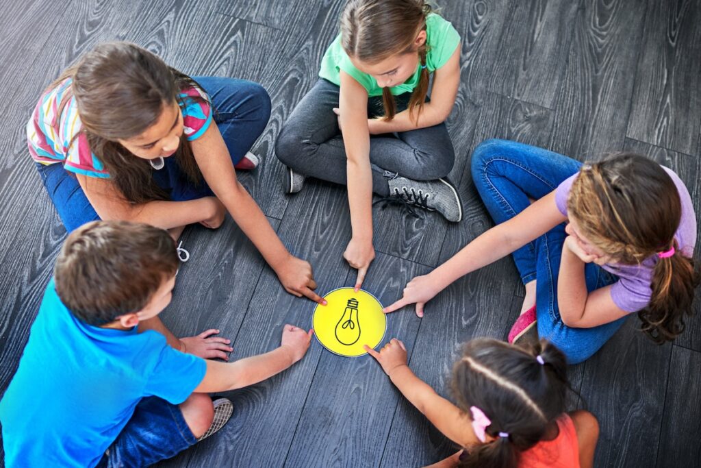 Дети, указывающие пальцем и играющие на полу с лампочкой, принятие решений и обучение. Круг многообразия, люди и решение проблем с помощью образовательной деятельности, решения и знания в обзоре сверху.