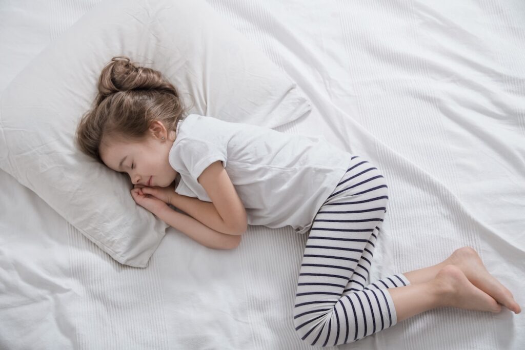 Cute little girl with long hair sleeping in a white crib. Concept of sleep and child development. Top view.