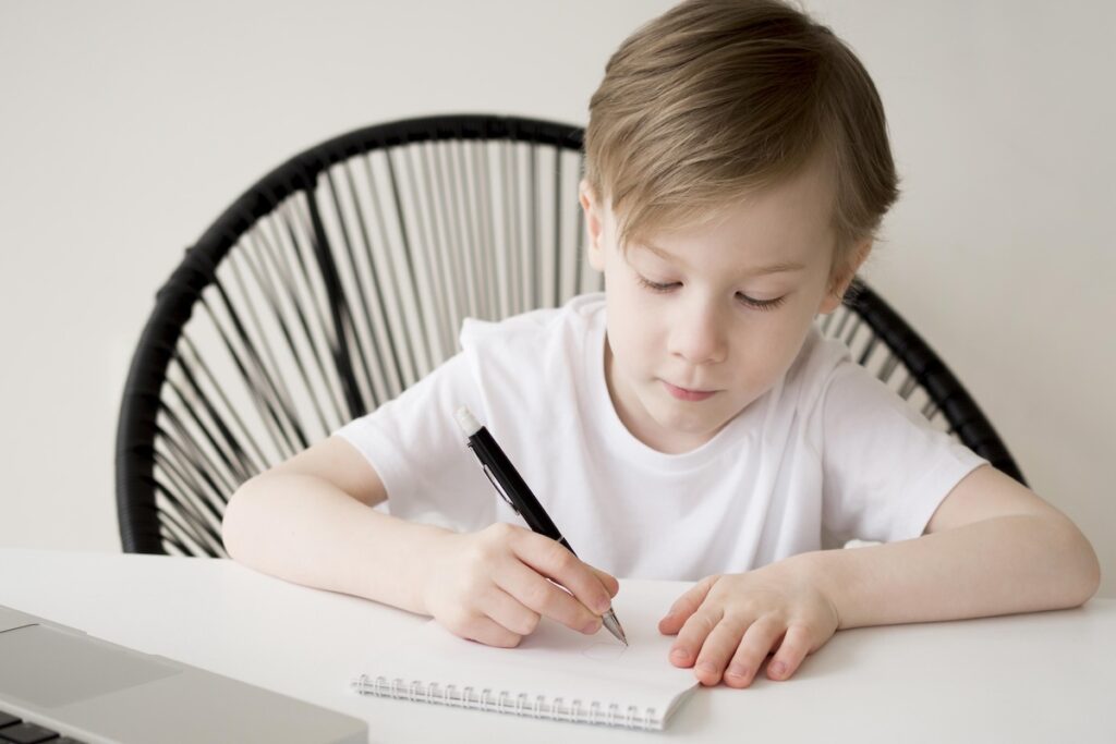 Мальчик пишет на тетради ручкой