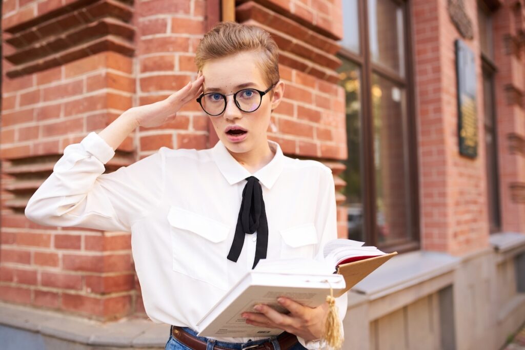 Красивая женщина в очках гуляет по городу, демонстрируя книжное образование. Фотография высокого качества.