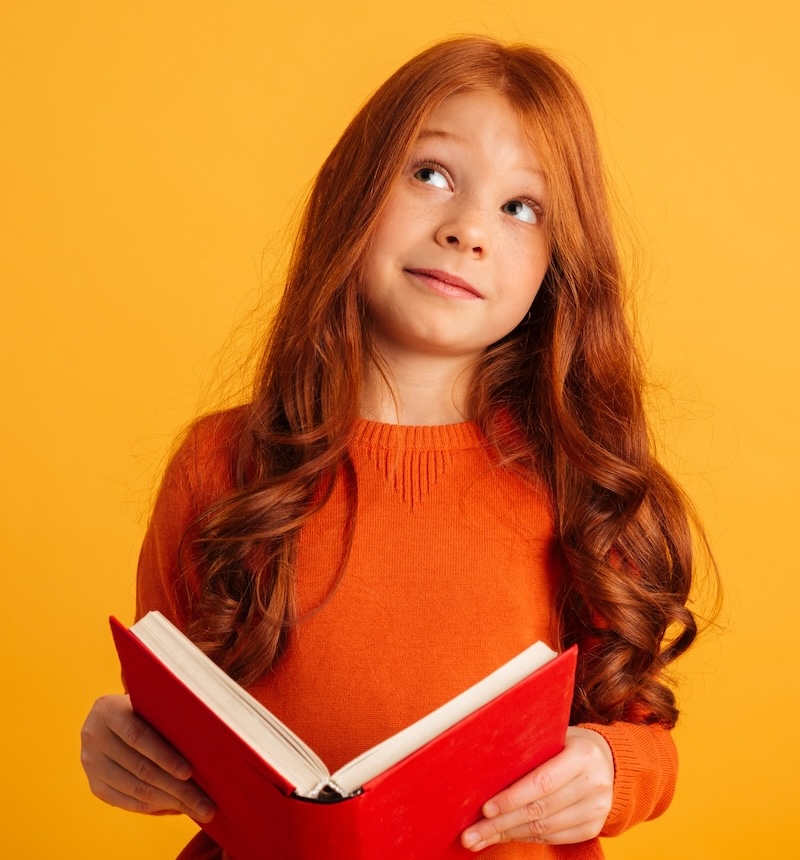 Задумчивая рыжеволосая девочка читает книгу