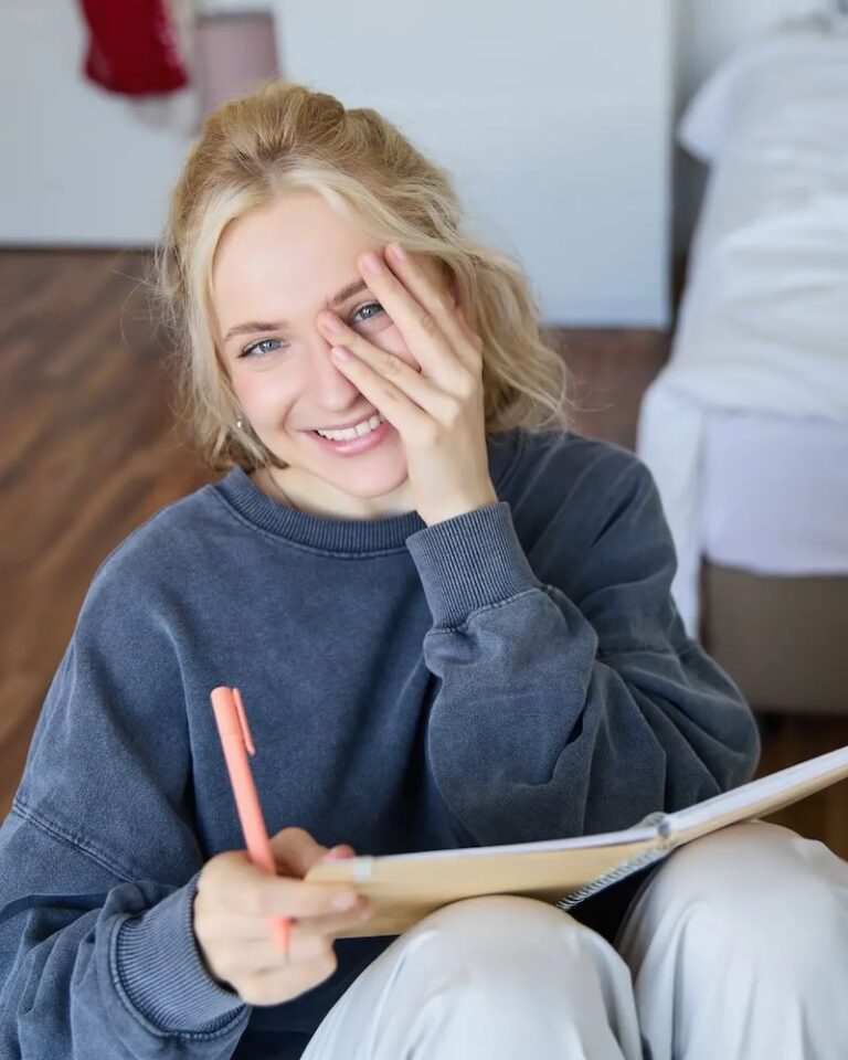 A girl sits with a notebook and pen on the floor