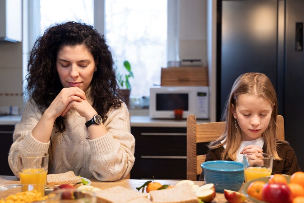 Мама и девочка за столом читают молитву