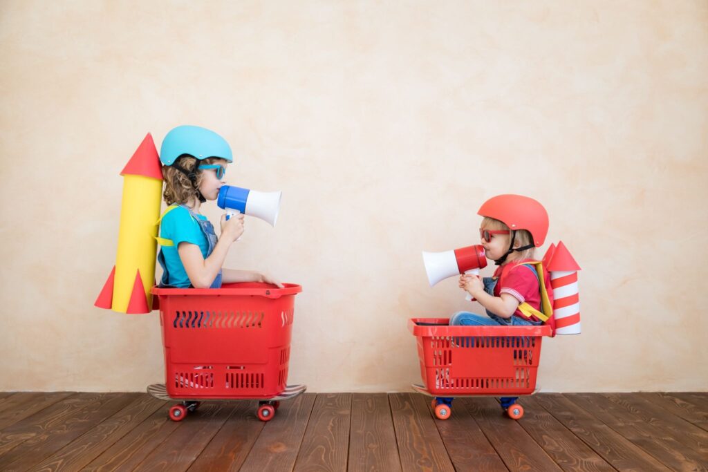 Two children are sitting in grocery carts, helmets