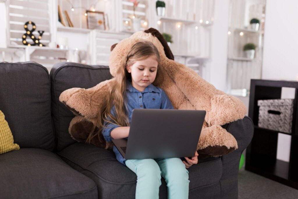 A girl is sitting on the sofa with a laptop on her lap.