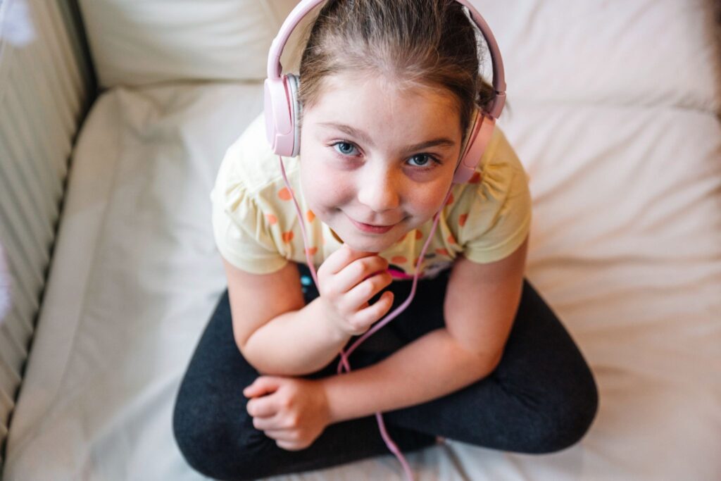 The girl is sitting, wearing headphones