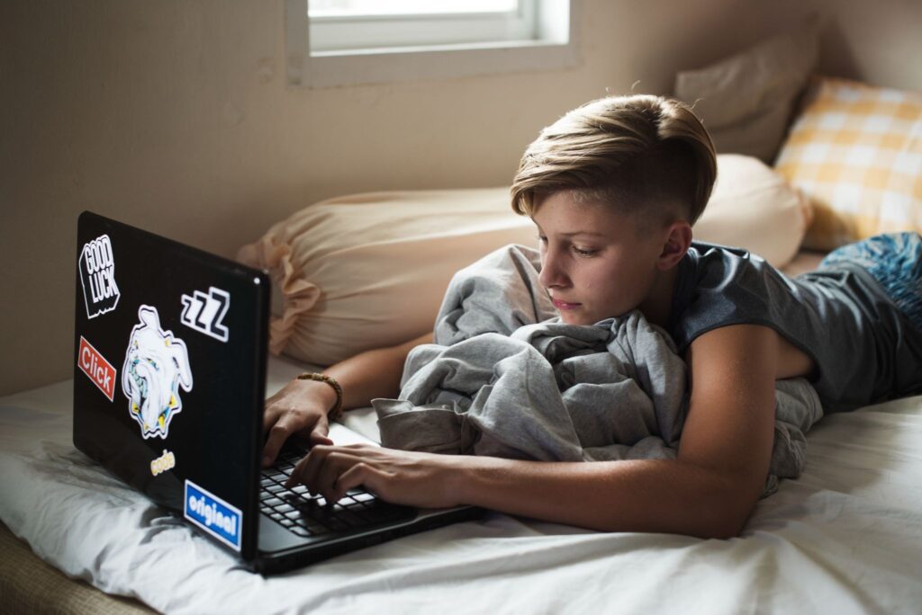 Мальчик лежит на кровати с ноутбуком.