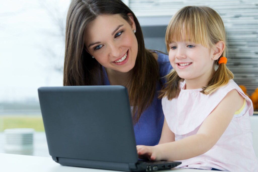 Мама и девочка улыбаются и смотрят в ноутбук