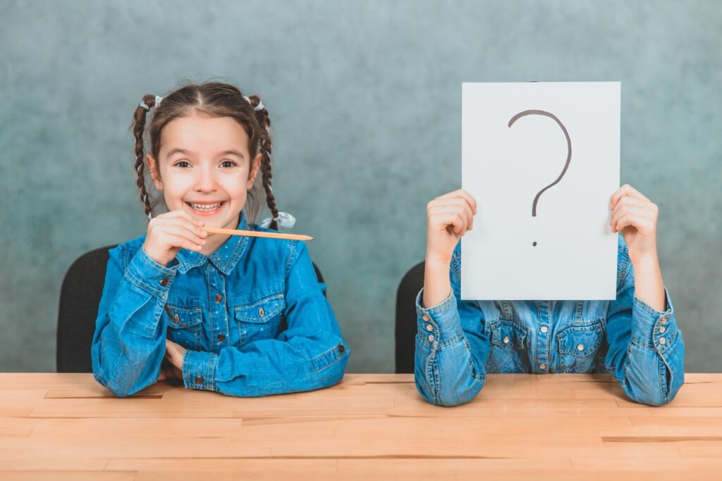 Двое детей, Девочка с карандашом показывает на 2 ребенка, у которого лицо закрыто бумагой со знаком вопроса