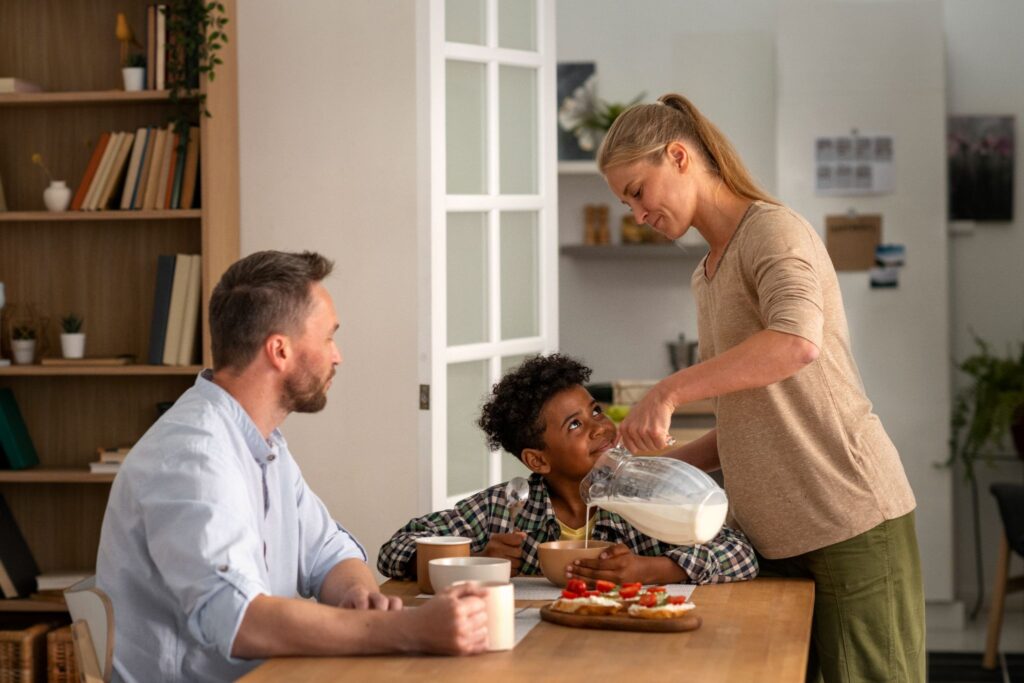 Папа и сын за столом смотрят, как мама наливает молоко