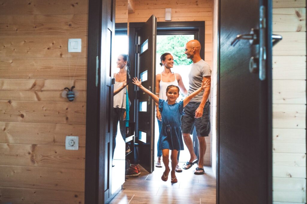 Радостная девочка с поднятыми руками вверх бежит вперед, на заднем плане 2 взрослых