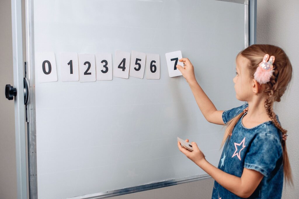Девочка крепит к доске карточки с числами