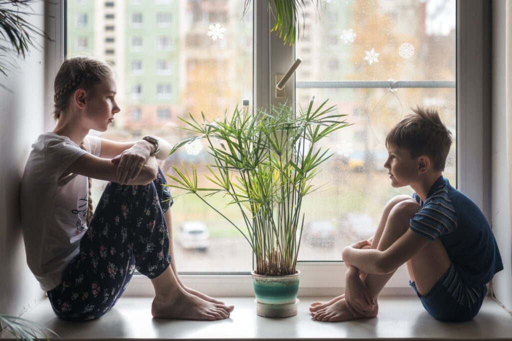 Девочка и мальчик сидят друг на против друга на подоконнике