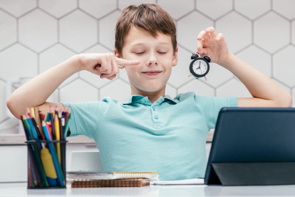 The boy is holding a watch and pointing to it with his other hand.