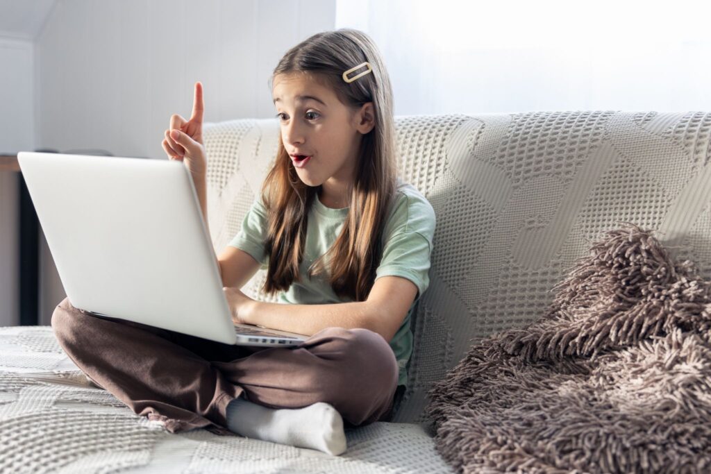 A girl is sitting on a couch with a laptop on her lap.