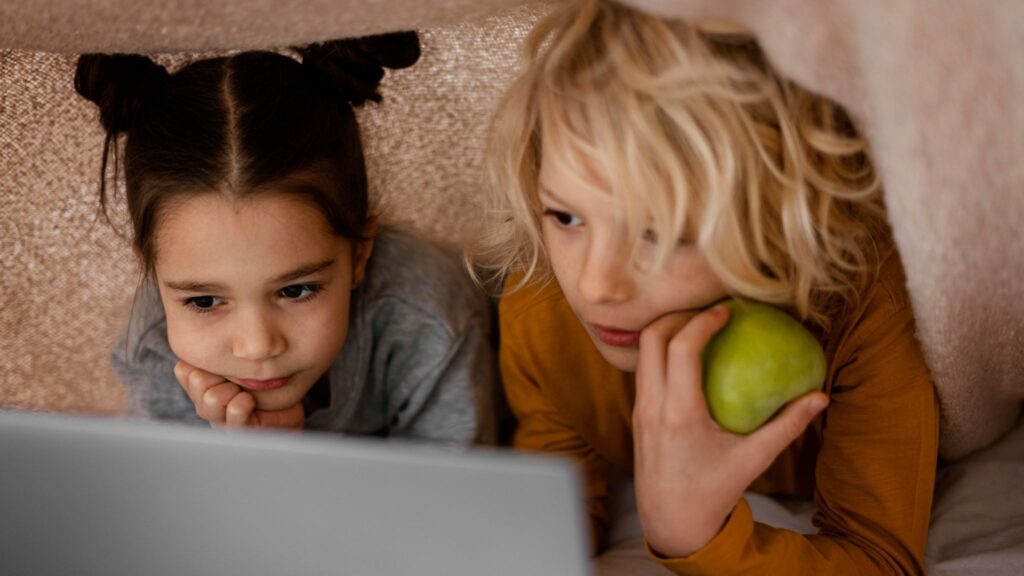 Two children under a blanket are looking at a laptop