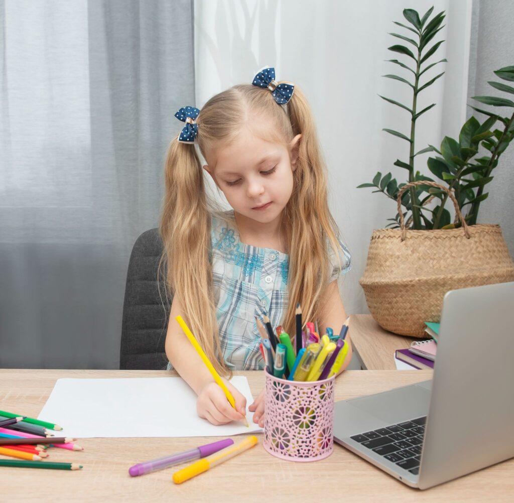 Девочка за столом с карандашами что то пишет
