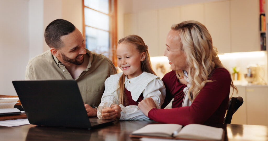 Mom, daughter, and dad at a table with a laptop, all smiling