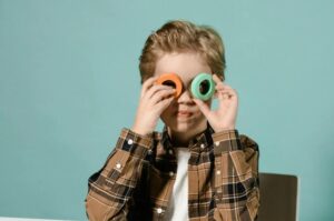 The boy is holding two multicolored plastic circles up to his eyes.