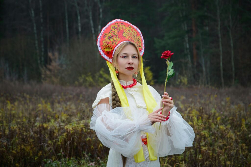 A girl in a field wearing a kokoshnik and holding a rose