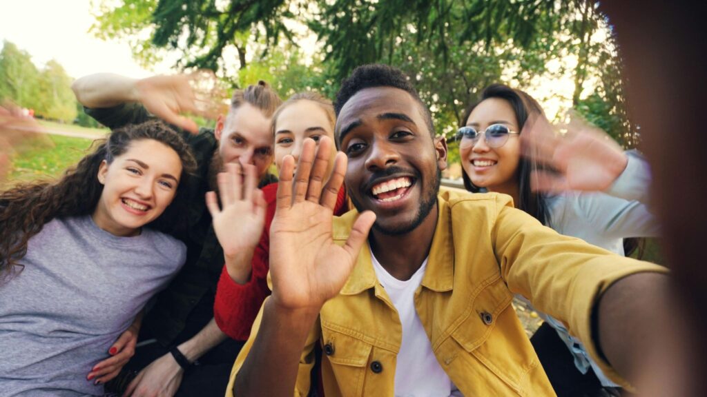 Five young people are smiling and waving at the camera.