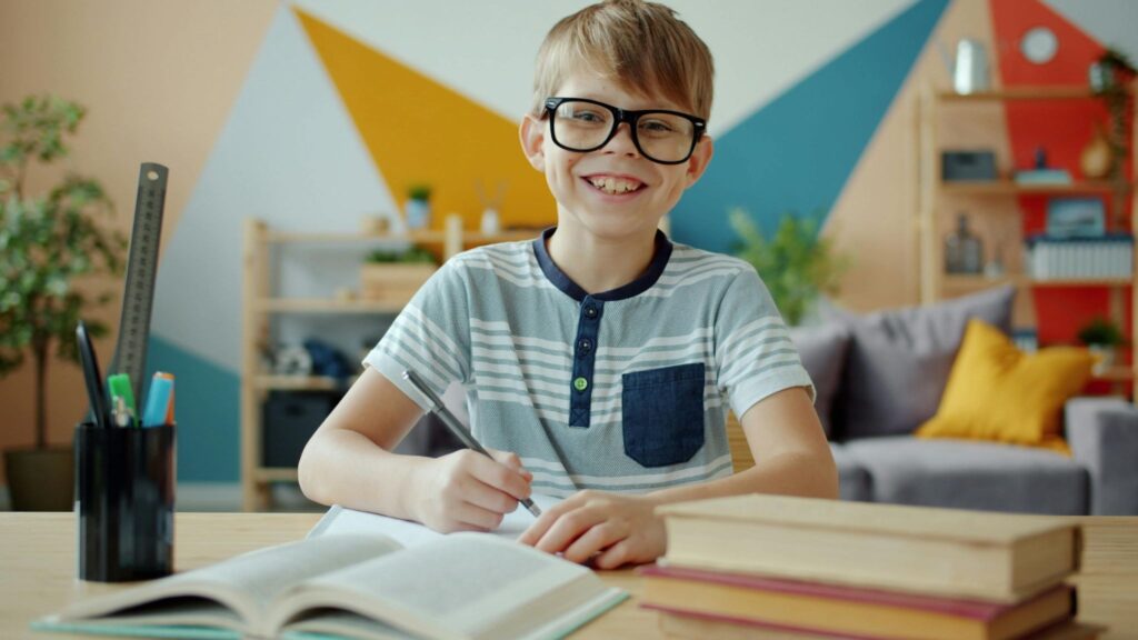 A boy at a table with a pen, notebooks, and books