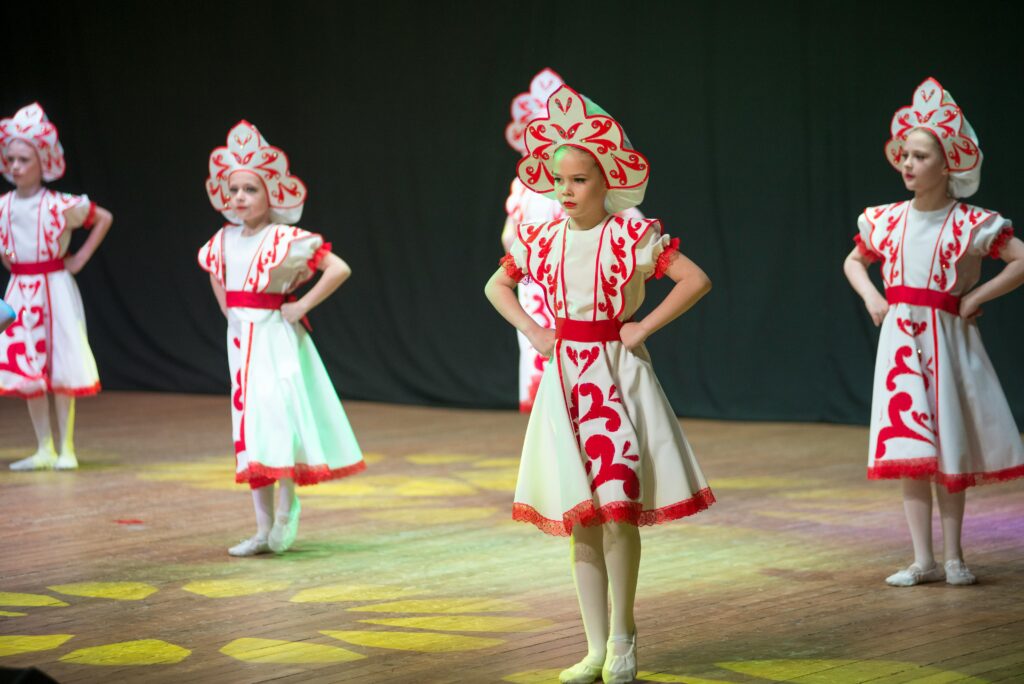 Children on stage in white and red dresses and kokoshniks