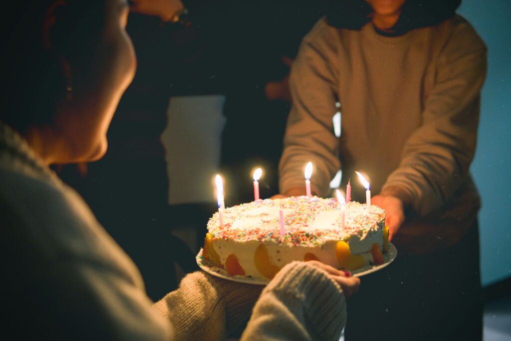 A warm and festive indoor birthday scene featuring a colorful cake with lit candles.