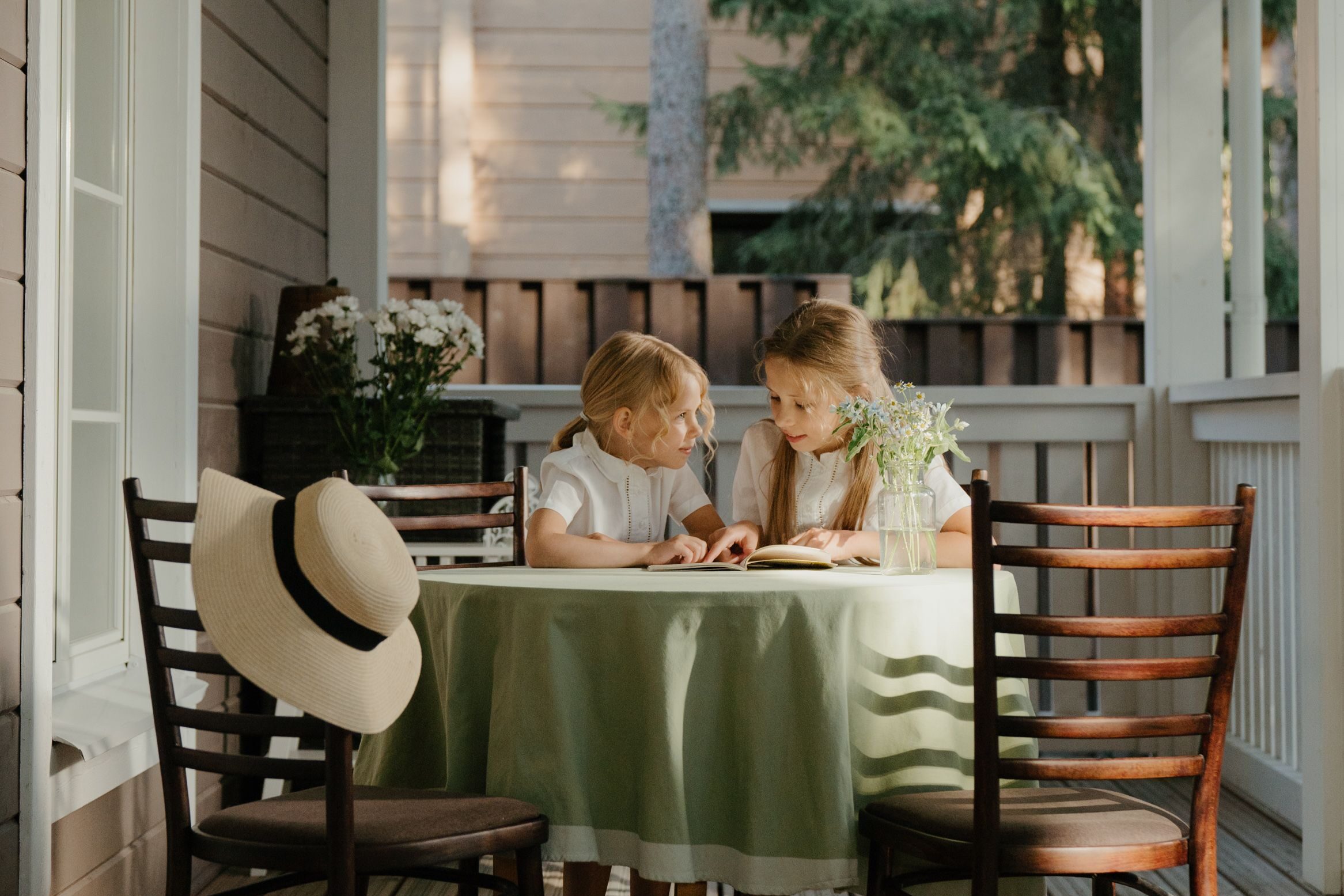 Two little girls discussing some interesting part of a book while sitting at a table outside