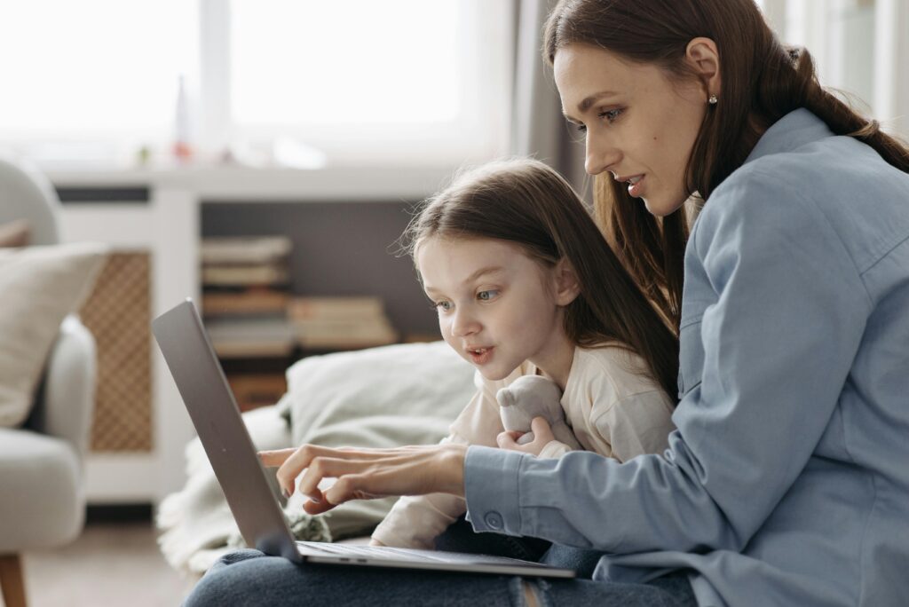 A mother and a daughter are reading something from the screen of a laptop